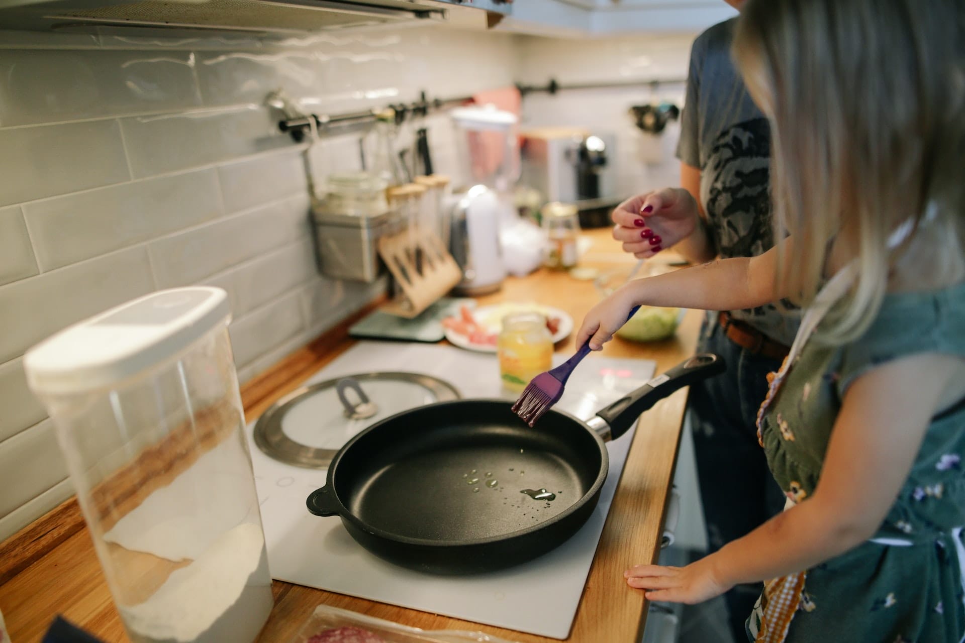 Two people preparing food in kitchen using pan