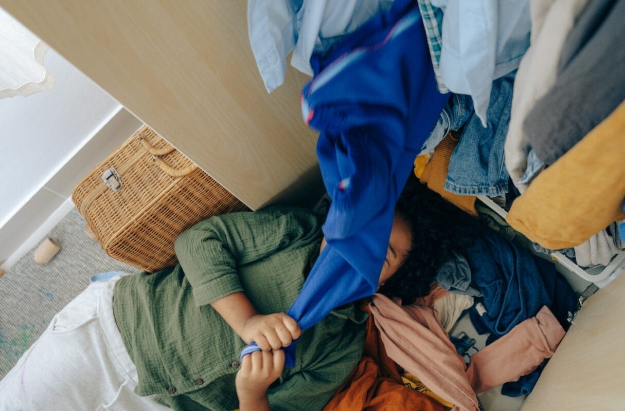 girl lying in a stack of clothes in bedroom